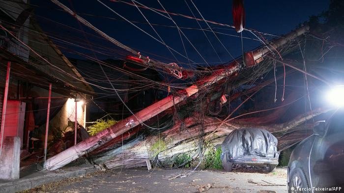 Cena de destruição após ventos fortes, com árvores caídas e postes danificados em uma rua urbana afetada por fenômenos climáticos extremos em São Paulo, Sul, Sudeste causados por esses desastres naturais.