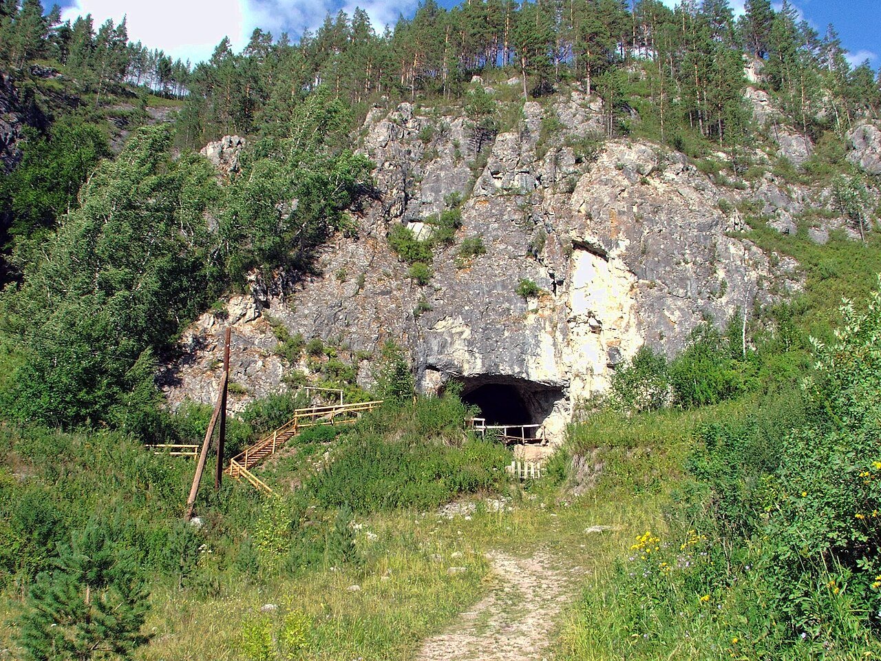 Entrada da Caverna de Denisova localizada em uma encosta rochosa cercada por árvores nas Montanhas Altai, Sibéria. Povo Denisovano. Superpoderes. Genética.